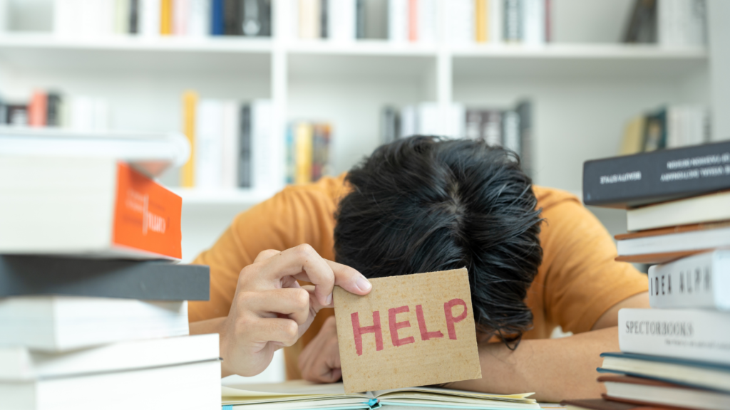 An office worker with their head down, holding a help sign, symbolising the struggle of social anxiety and how public speaking training can build confidence and communication skills.